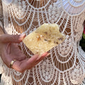 Hand with a gold ring holding Copal Blanco (also known as White Copal) against a textured white lace shirt background